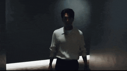 a man in a white shirt and black pants is standing in a dark hallway .