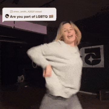 a woman is dancing in front of a sign that says ' lgbtq ' on it