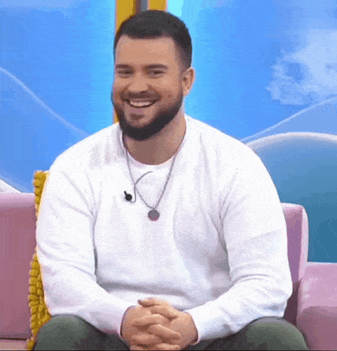 a man with a beard is smiling while sitting on a couch .