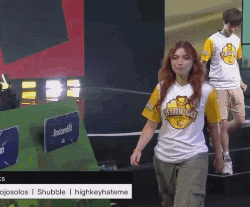 a man and a woman wearing yellow kings shirts walk on stage