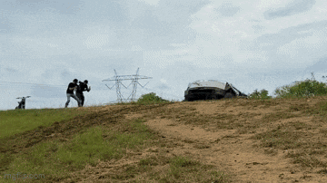 a couple of people standing on top of a grassy hill with a car in the background
