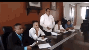 a group of people are sitting around a table in a conference room .