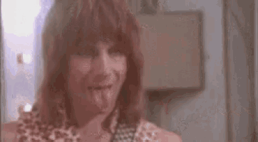 a man with long hair is sticking his tongue out and holding a guitar .