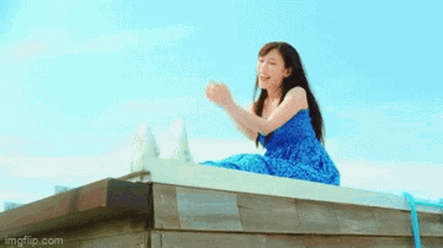 a woman in a blue dress is sitting on the edge of a building