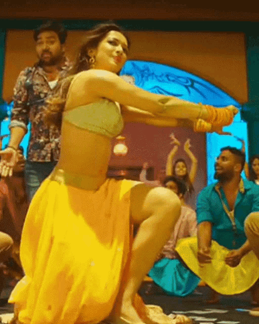 a woman in a crop top and yellow skirt is dancing in front of a crowd