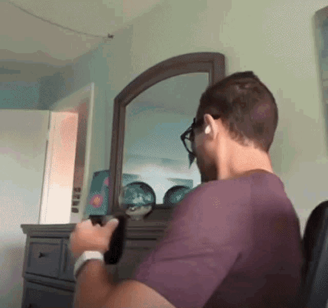 a man in a purple shirt is looking at his reflection in a mirror .