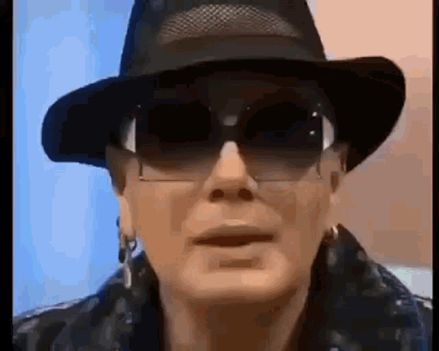 a woman wearing a hat and sunglasses is making a face .