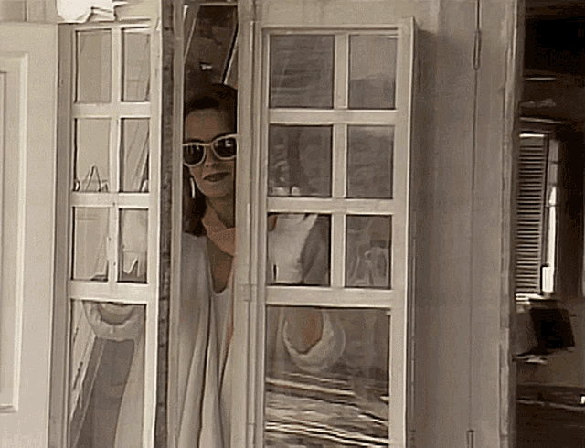 a woman wearing sunglasses looks out of a doorway
