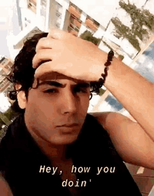 a man with a bracelet on his wrist is holding his hand to his forehead and making a funny face .