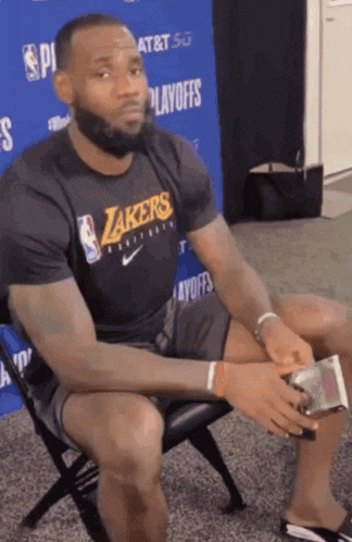 a man in a lakers shirt sits on a chair