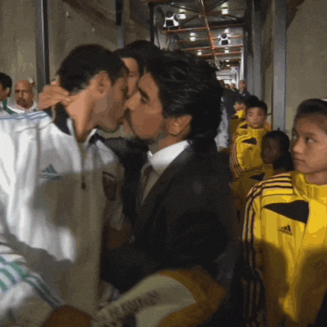 a man in a white adidas jacket is kissing another man