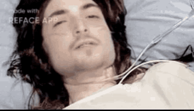 a man with long hair and a beard is laying in a hospital bed with a tube in his neck .