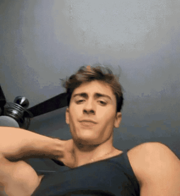 a man in a black tank top is standing in front of a ceiling fan in a room .