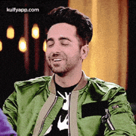 a man wearing a green jacket and a black shirt is smiling .
