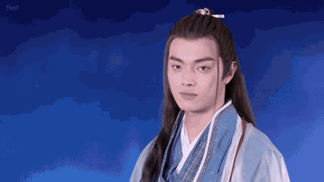 a young man with long hair is wearing a blue robe and a ponytail .
