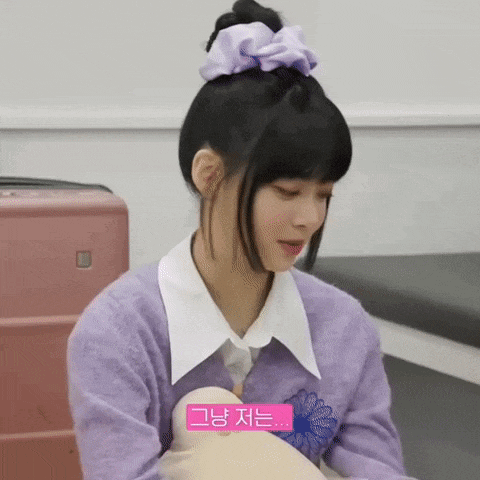 a woman in a purple sweater and a purple scrunchie is sitting in front of a pink suitcase .