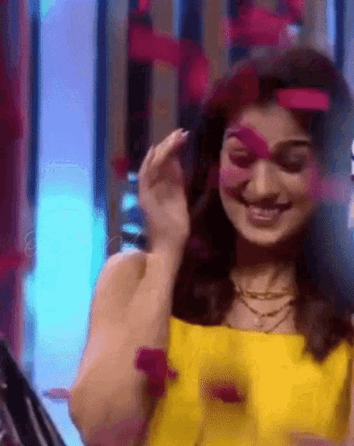 a woman in a yellow dress is smiling and holding a red flower in her hand .