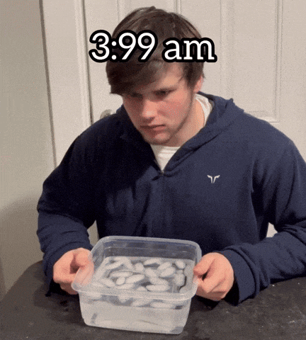 a man in a blue hoodie is holding a plastic container filled with ice cubes