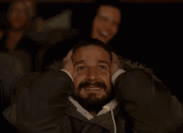 a man with a beard is sitting in a movie theater with his hands on his head .