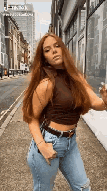 a woman with long red hair is standing on a sidewalk in front of a building .