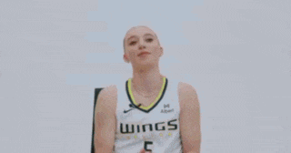 a woman is sitting in a chair and smiling while wearing a basketball uniform .