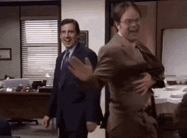 two men in suits and ties are dancing in an office