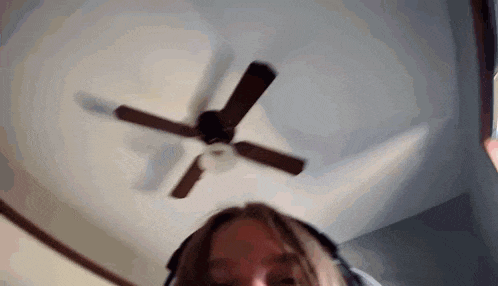 a woman wearing headphones is looking up at a ceiling fan in a room .