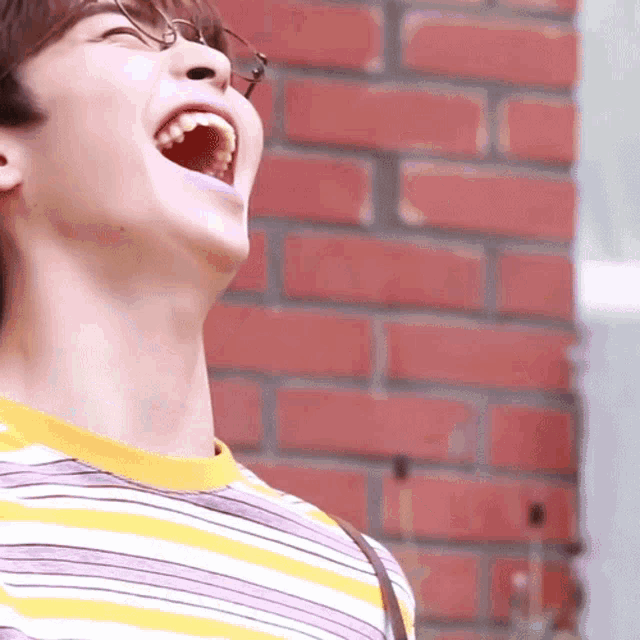 a young man wearing glasses is laughing with his mouth wide open