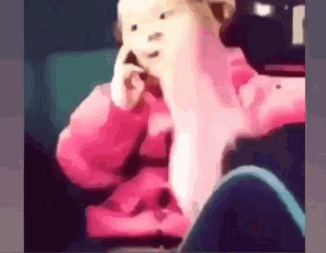a girl in a pink sweater is sitting in a chair talking on a cell phone