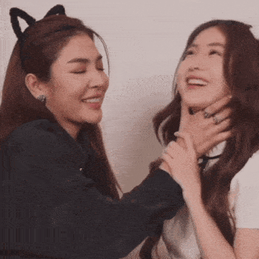 a woman wearing a cat ear headband holds another woman 's neck