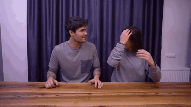 a man and a woman are sitting at a table with their hands on the table
