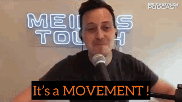 a man speaking into a microphone in front of a neon sign that says meiis toll