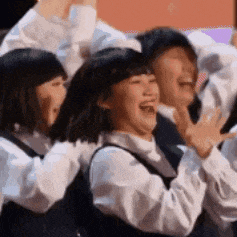 a group of people are standing next to each other laughing and raising their hands in the air .