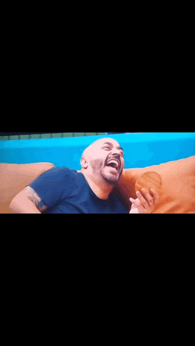 a bald man is sitting on a couch laughing .