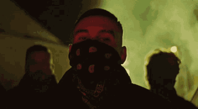 a man wearing a bandana on his face is standing in front of a crowd of people .