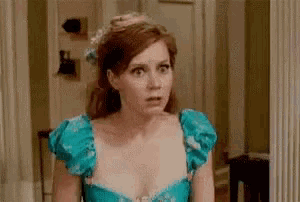 a woman in a blue dress is standing in front of a mirror making a surprised face .