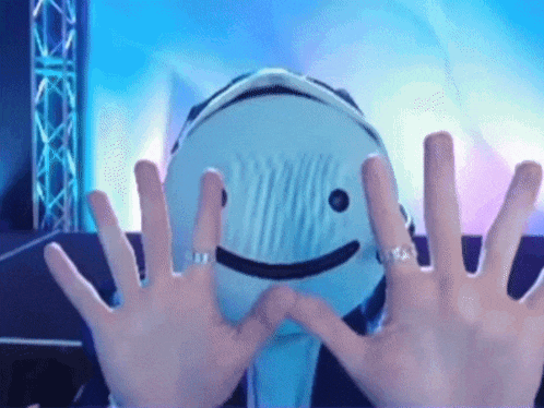 a person is making a heart with their hands in front of a mask with a smiley face on it