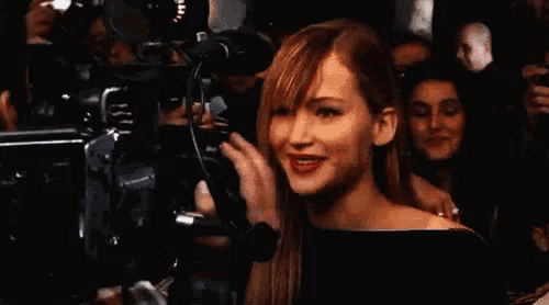 a woman stands in front of a camera in a crowd and smiles