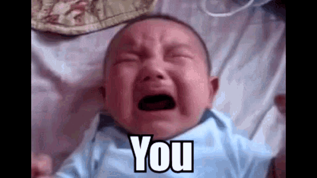 a baby is crying while laying on a bed and the baby is saying `` you '' .
