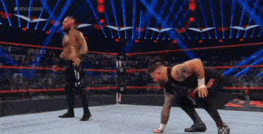 two men are wrestling in a wrestling ring and one of them is kneeling on the ground .