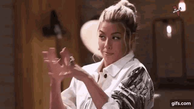 a woman is making a heart shape with her hands while wearing a white jacket .