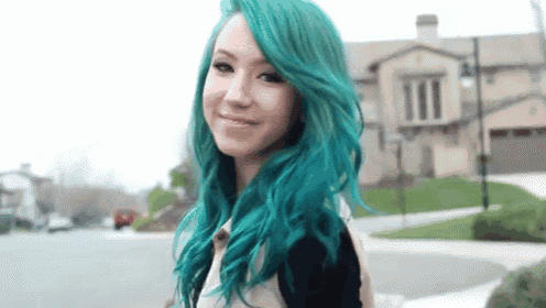 a woman with green hair is standing in front of a house on a street .