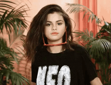 a woman wearing a black t-shirt with the word neo on it is standing in front of palm trees .