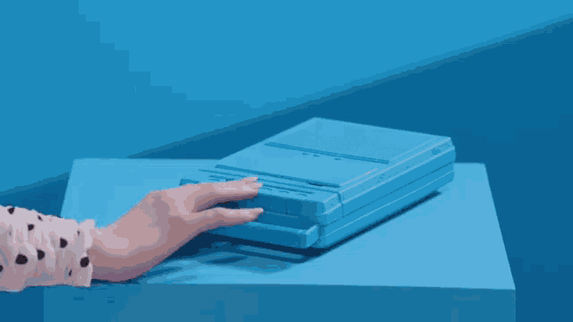 a woman 's hand is reaching into a blue box on a blue surface