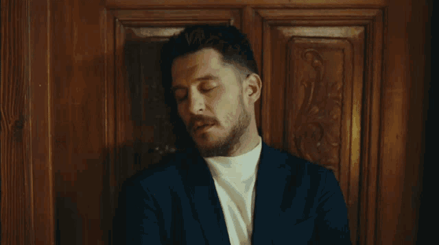 a man with a beard wearing a suit and white turtleneck