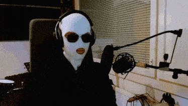 a person wearing a ski mask and headphones holds a microphone