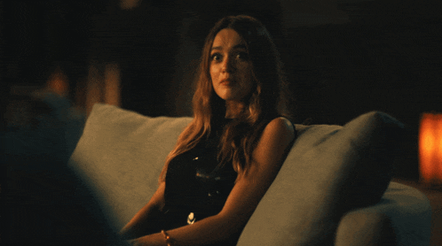 a woman in a black dress sits on a couch in a dark room