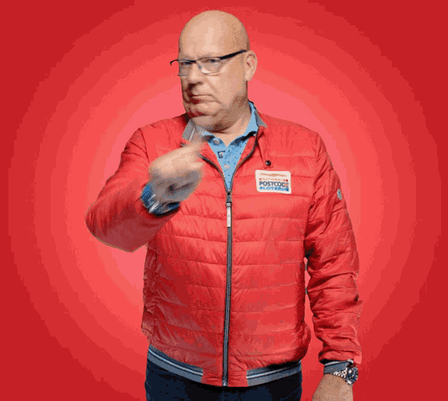 a man wearing a red jacket with a postcode sticker on it gives a thumbs up