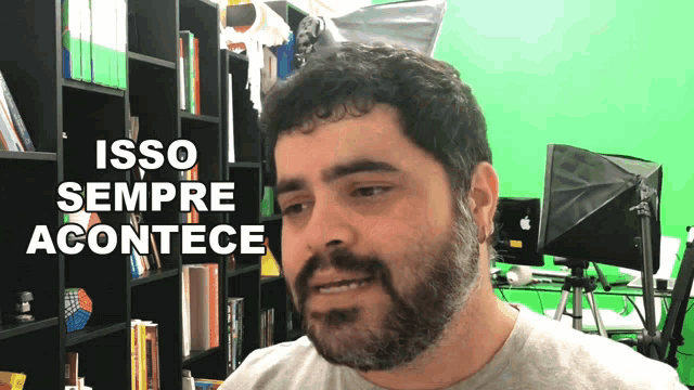 a man with a beard stands in front of a green screen with the words isso sempre acontece on it