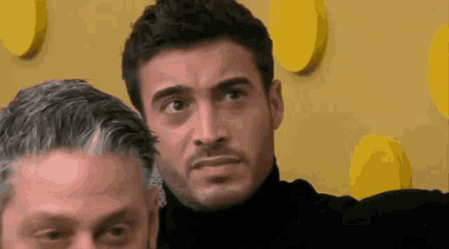 two men are standing next to each other and one is wearing a black turtleneck .
